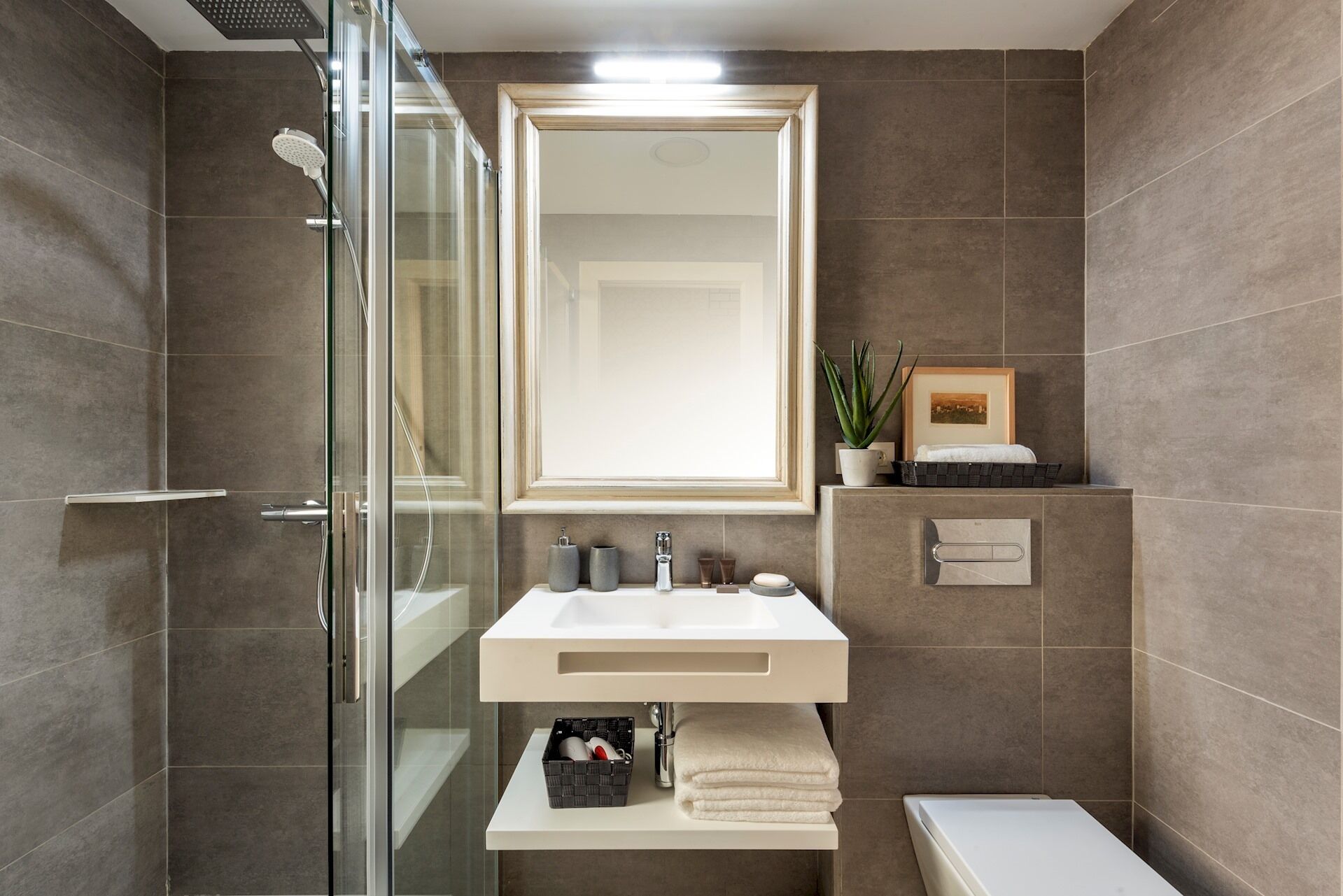 A modern bathroom with a glass shower enclosure, a white sink with a mirror above, and a small shelf with toiletries.