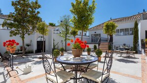 A courtyard with a round table and chairs, surrounded by potted plants and a white building with a tiled roof. - Genteel Home Carmen San Ignacio I (Granada)