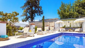 A swimming pool with tiled blue edges, surrounded by lounge chairs and umbrellas, with trees and a building in the background. - Genteel Home Carmen San Ignacio I (Granada)