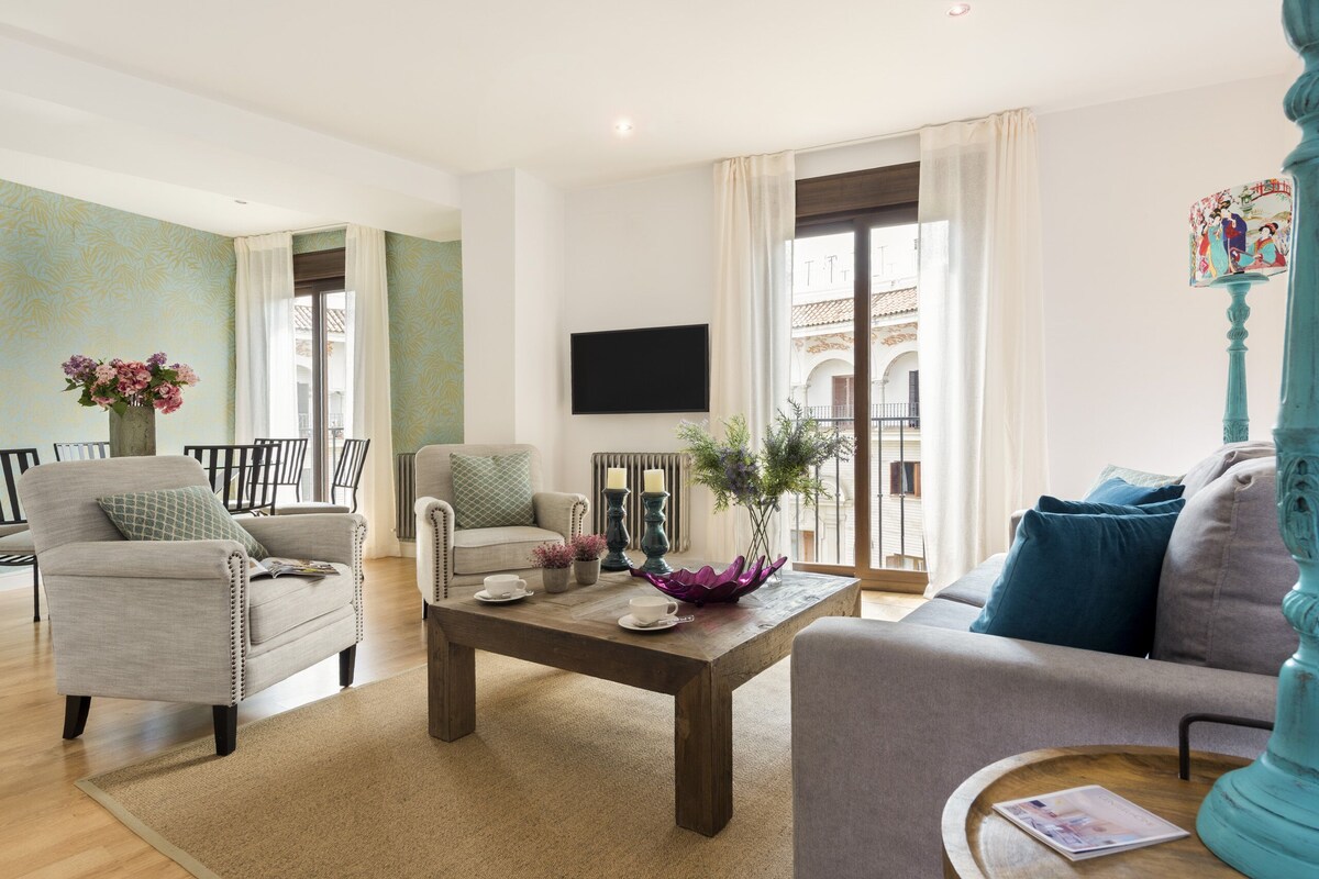 A living room with a sofa, armchairs, a coffee table, and a TV mounted on the wall.