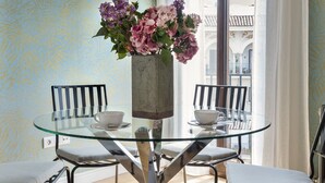 A dining area with a glass table, two chairs, a vase with flowers, and a view of a building through a window. - Genteel Home Cabildo III (Seville)