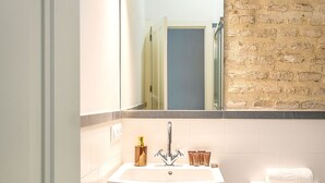 A bathroom with a white sink, a mirror, a toilet, and a brick wall. - Genteel Home Galera III (Seville)