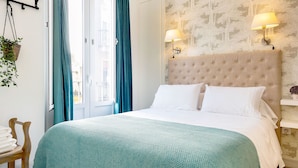 A neatly made bed with a teal bedspread, a wooden chair with folded towels, and a wall-mounted lamp. - Genteel Home Galera III (Seville)