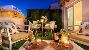 An outdoor seating area with white chairs and a table set for dining, featuring candles and a bottle of wine. - Genteel Home Galera III (Seville)