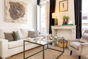 A living room with a white sofa, a glass coffee table, a fireplace, and a painting on the wall. - Genteel Home Galera III (Seville)
