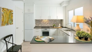 A compact kitchen with white cabinets, a built-in oven, and a small dining area with a table and chairs. - Genteel Home Plaza de las Flores (Málaga)