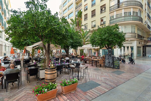 An outdoor café with tables and chairs, surrounded by trees and buildings.