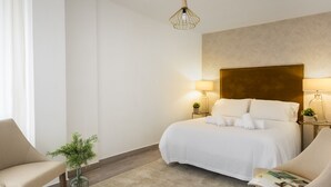 A hotel room with a large bed, two bedside lamps, a small table with a plant, and a chair. - Genteel Home Plaza de las Flores (Málaga)