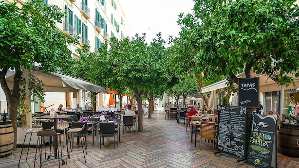 An outdoor café area with tables and chairs, surrounded by trees and covered by umbrellas. - Genteel Home Plaza de las Flores (Málaga)