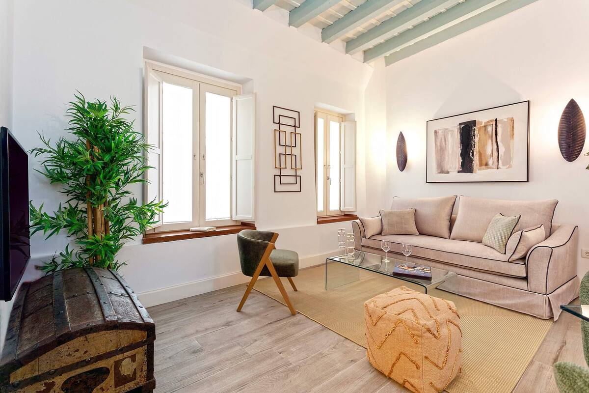 A living room with a sofa, a glass coffee table, a wooden chest, a green plant, and a modern art piece on the wall.