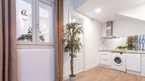 Una cuina moderna amb rentadora, una planta en test i una finestra amb cortines.