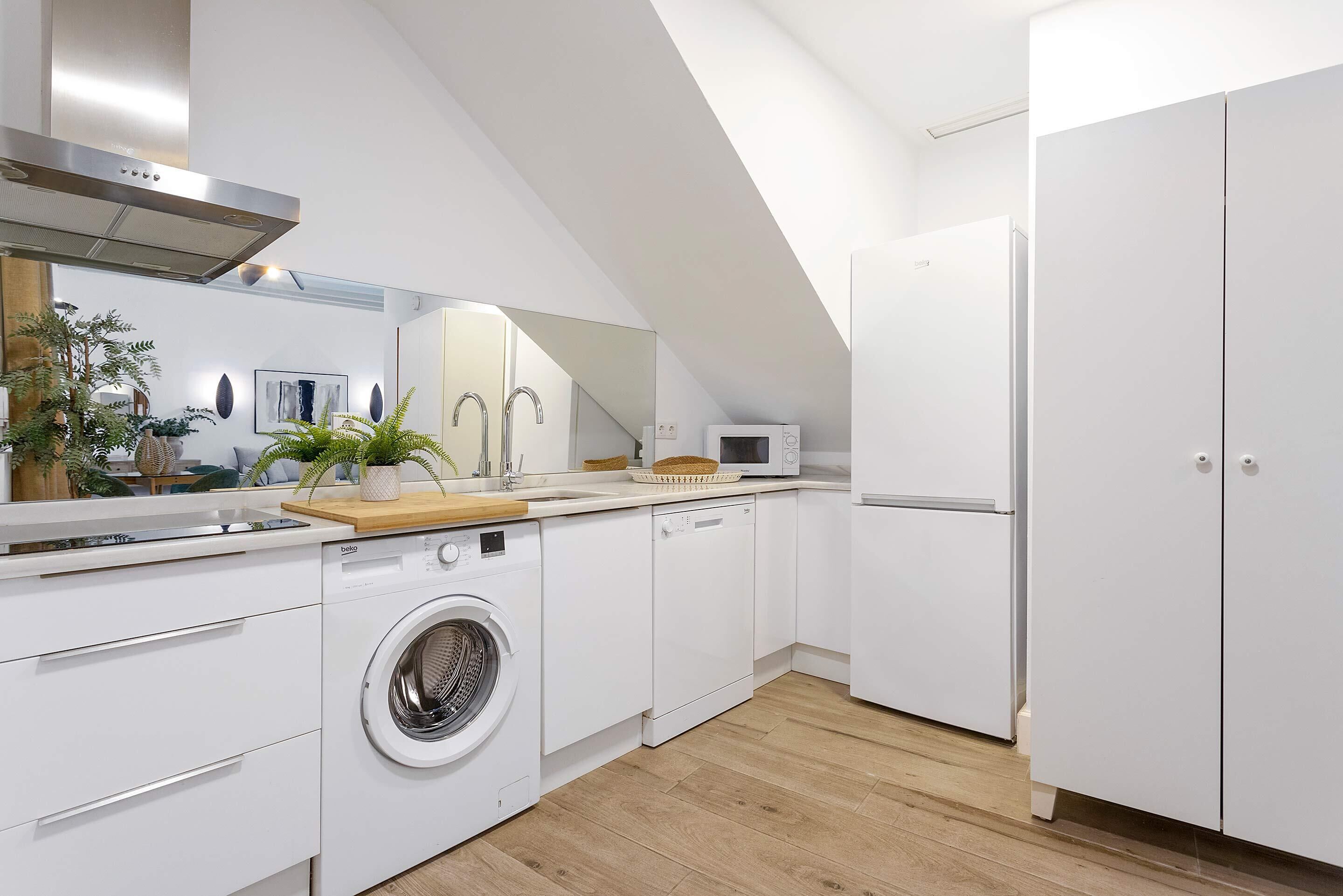 A modern kitchen with a washing machine, microwave, and white cabinets.