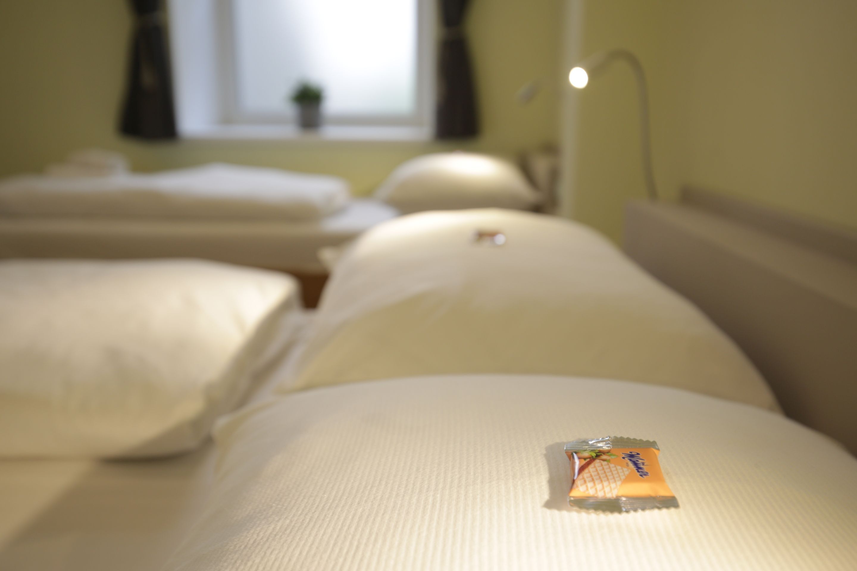 A hotel room with a bed, pillows, and a window with curtains.
