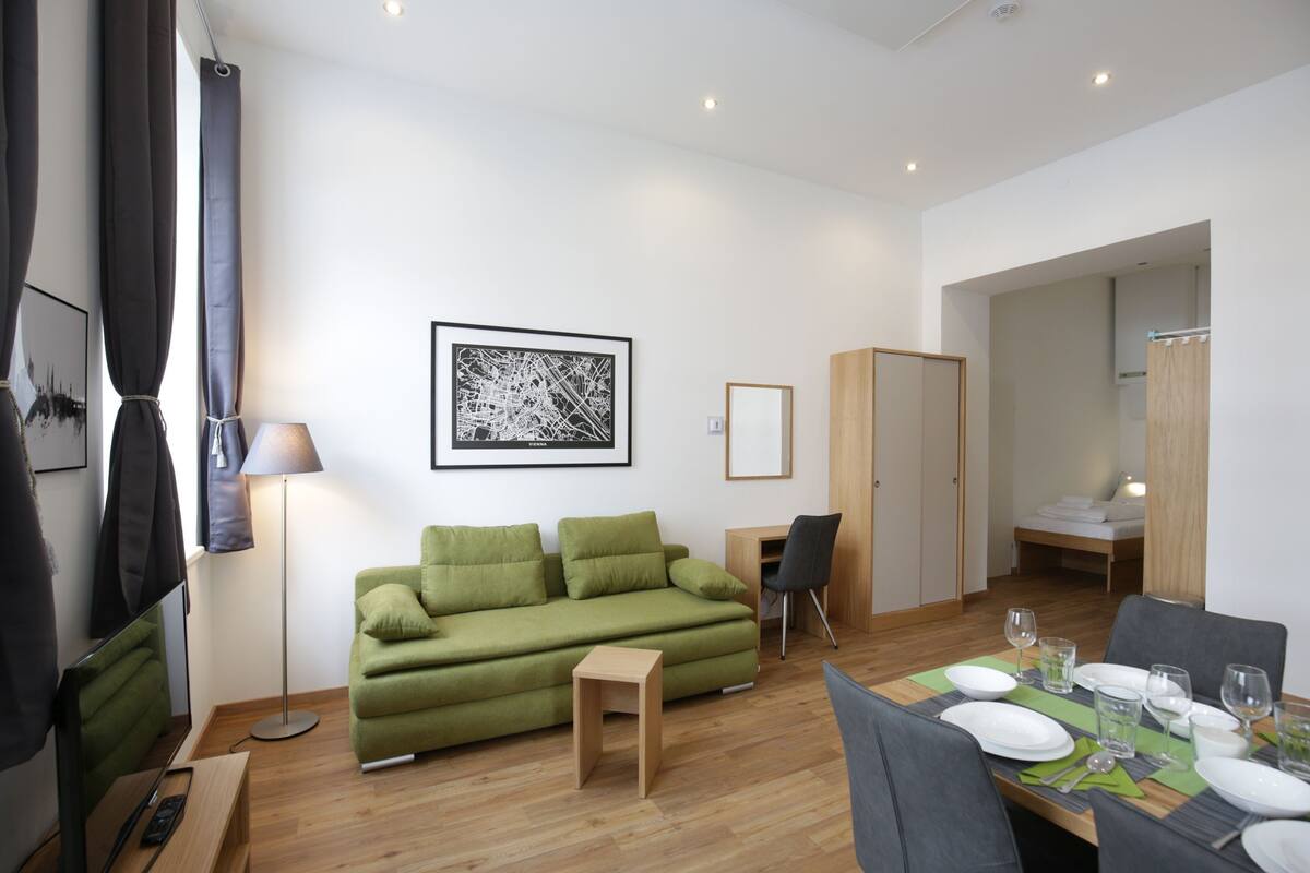 A modern living room with a green sofa, a small wooden table, and a dining area set for four.