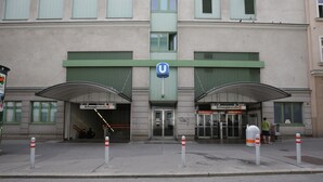 Um edifício com entrada em formato de U, toldo verde e defensas na calçada.