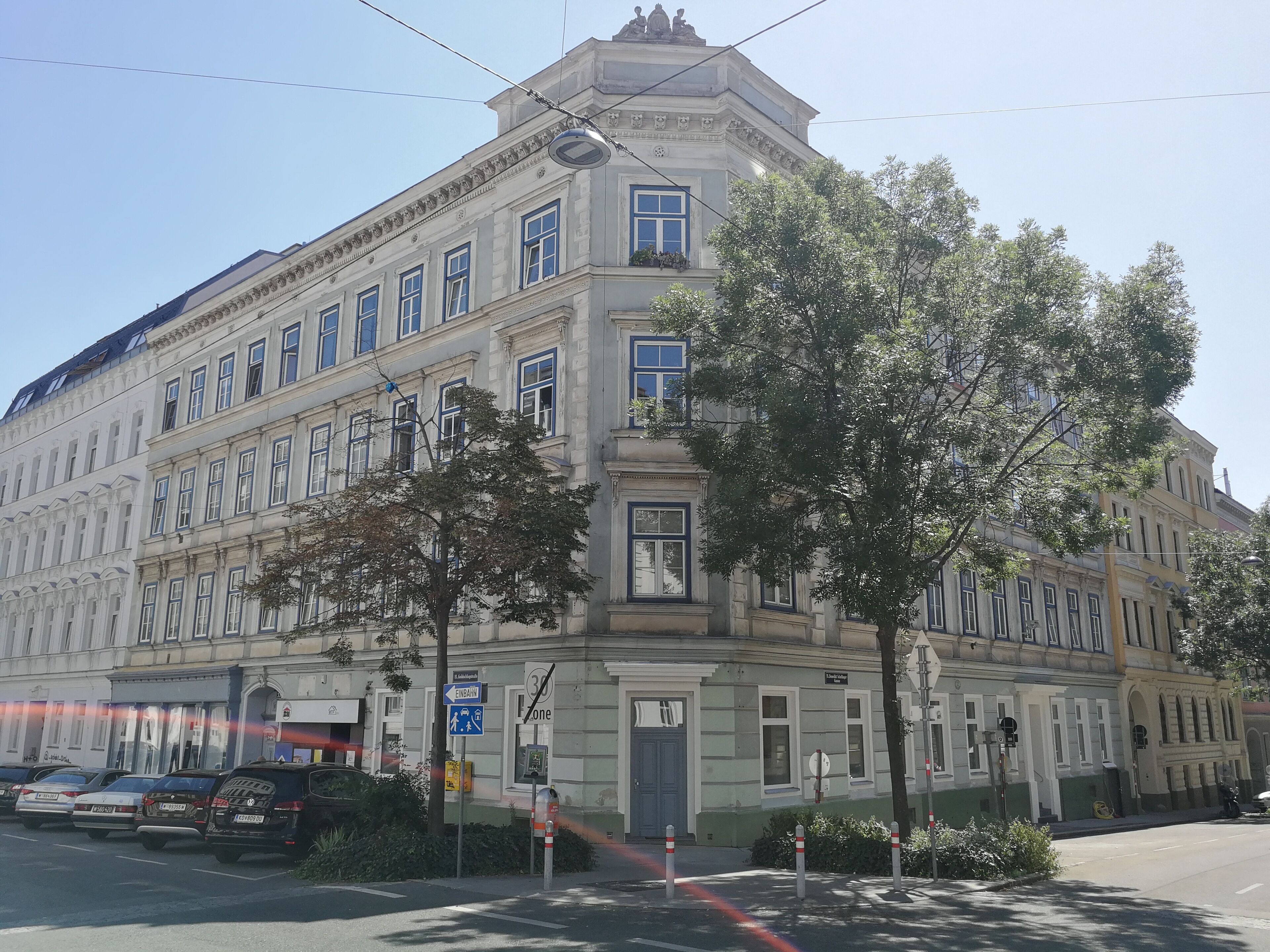 A multi-story building with classical architecture, featuring a corner entrance, large windows, and a prominent entrance door.