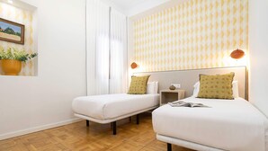 Ein Hotelzimmer mit zwei Betten, Holzboden, einer Wandlampe und einem Fenster mit Vorhängen.