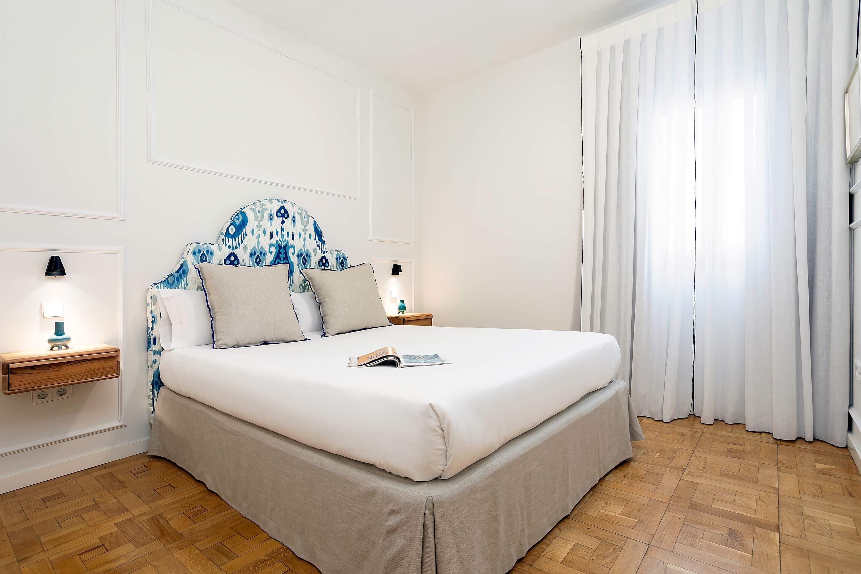 A neatly arranged bedroom with a bed, bedside tables, and a window with curtains.