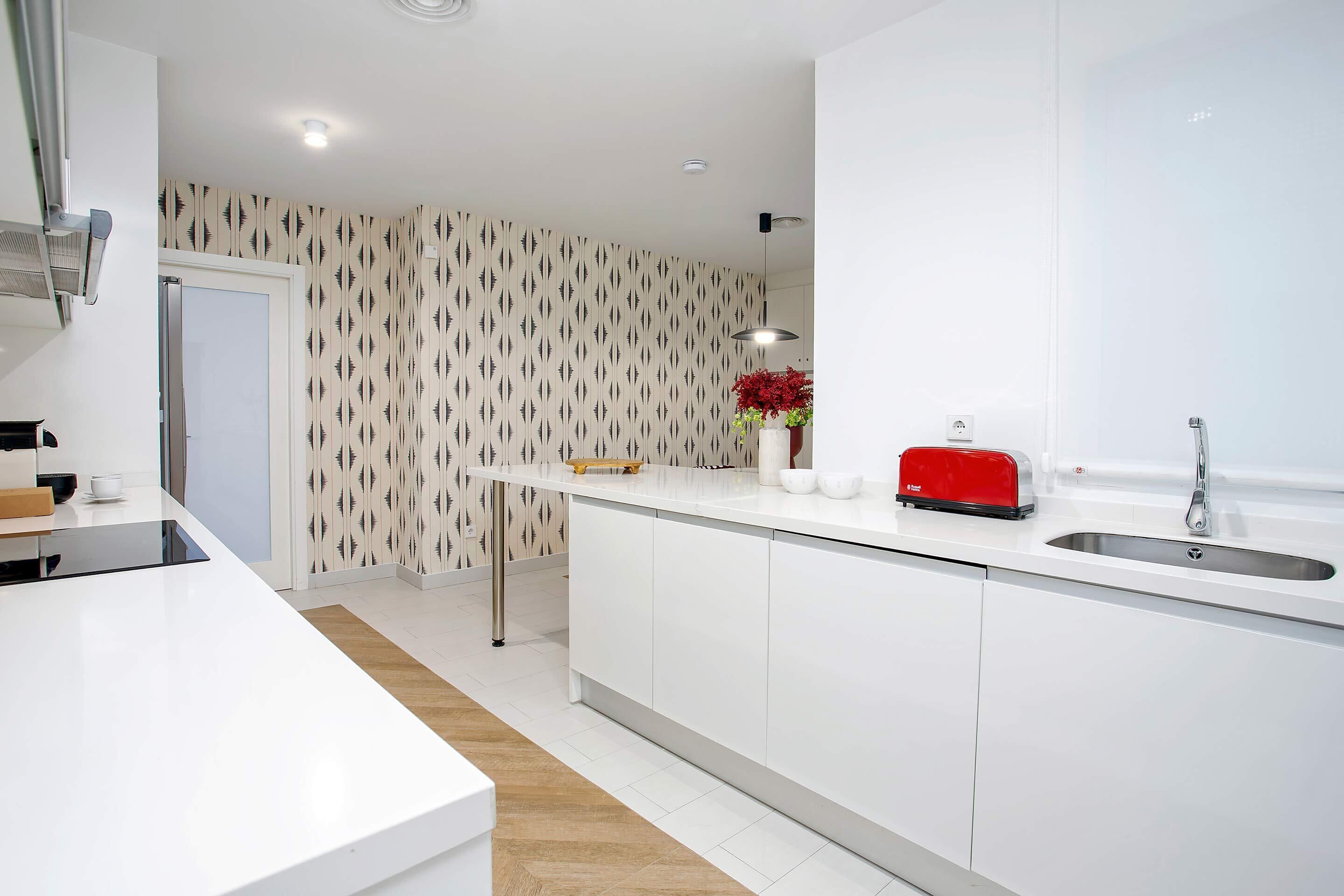 Una cocina moderna con armarios blancos, un lavamanos de acero inoxidable y un tostador rojo.