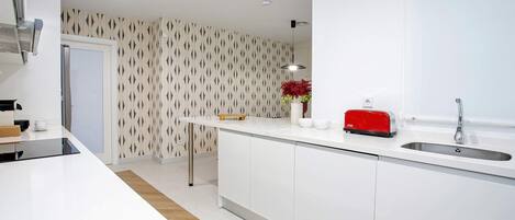 Una cocina moderna con armarios blancos, un lavamanos de acero inoxidable y un tostador rojo.