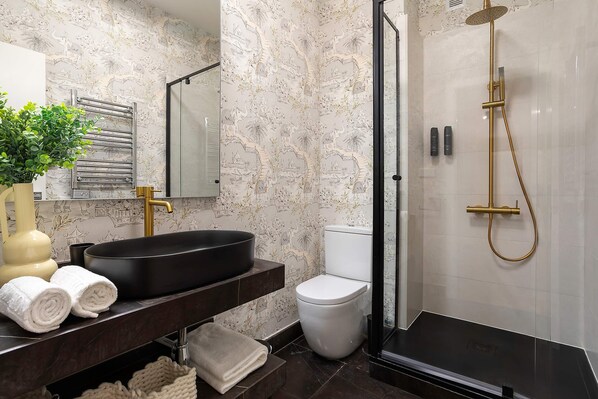 A bathroom with a black sink, white toilet, and a gold showerhead. - Genteel Home Cabildo IV (Seville)