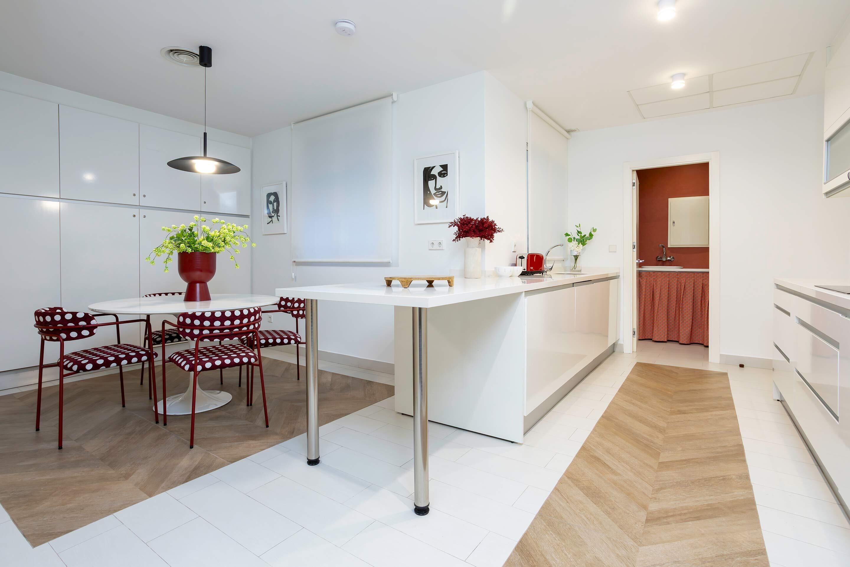 A modern kitchen with white cabinetry, a dining area with red chairs, and a central island with a potted plant.