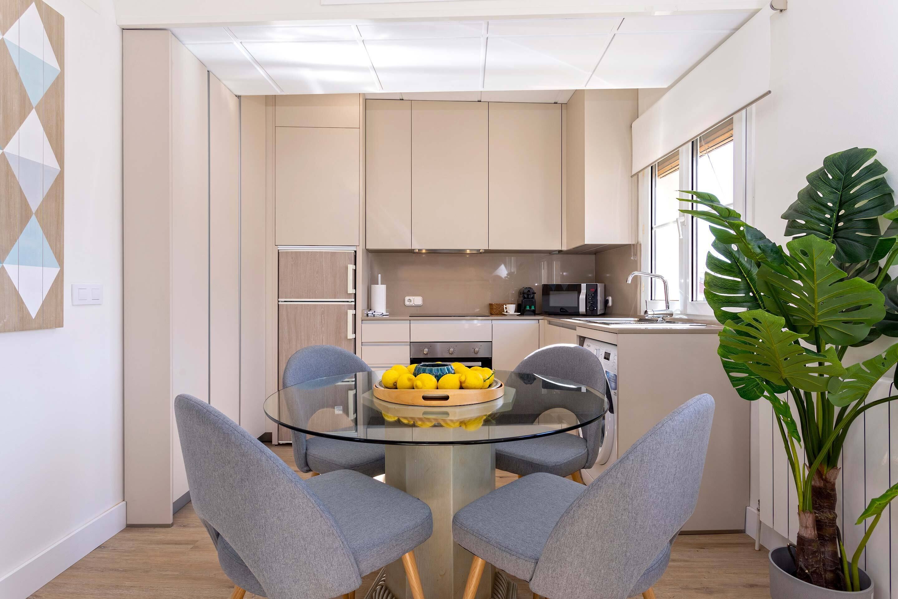 Une cuisine moderne avec une table à manger en verre, des chaises grises et une plante en pot.
