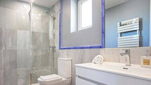 Un baño moderno con cabina de ducha de vidrio, inodoro blanco y lavamanos con espejo.