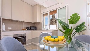 Una cocina moderna con una mesa de comedor de vidrio, dos sillas, un cuenco de limones y una planta grande.