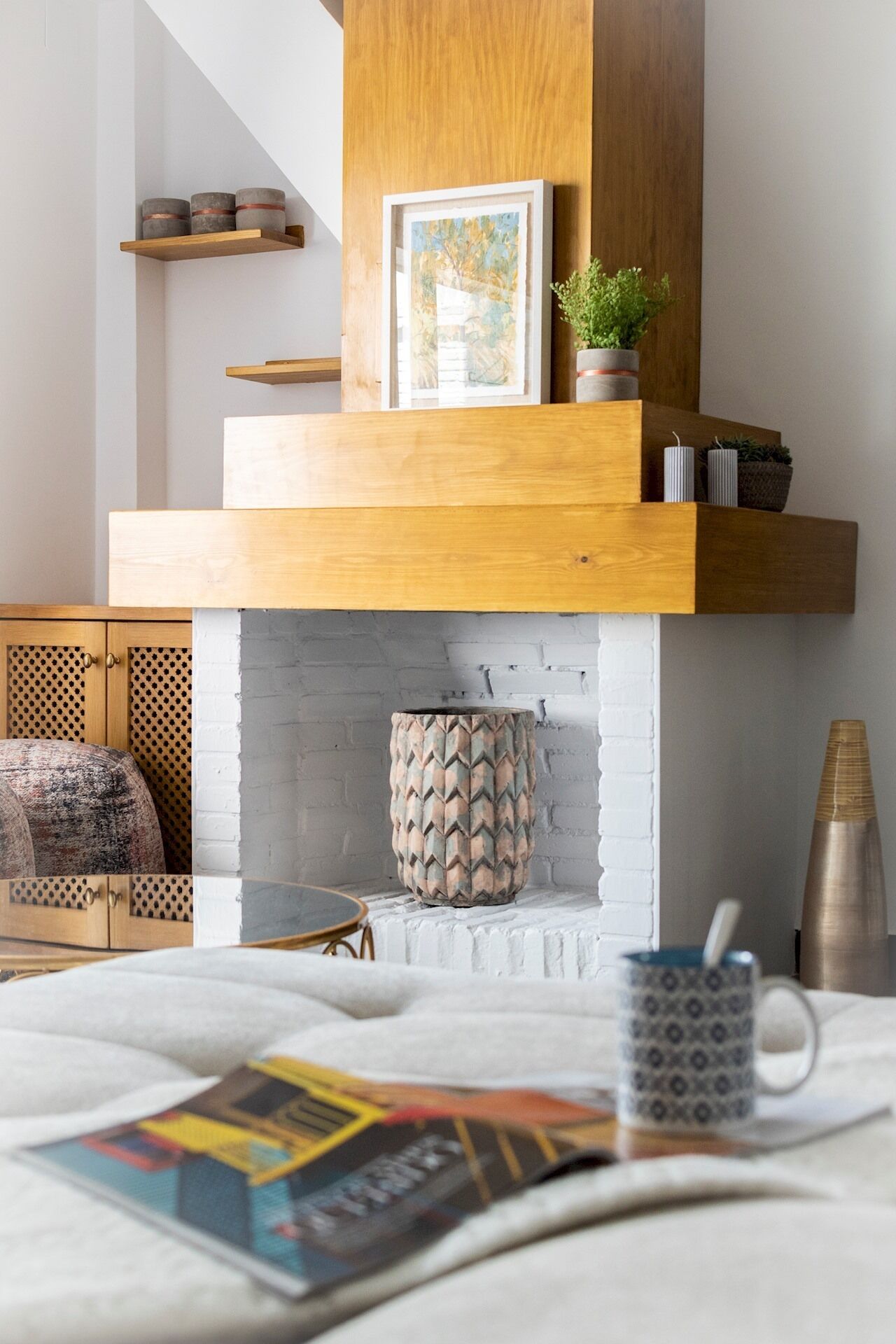 Un salon moderne avec une cheminée, des étagères en bois, un tableau encadré et une plante en pot.