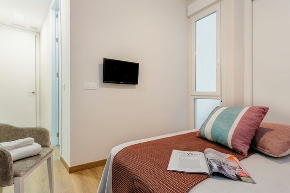 A bedroom with a bed, a television on the wall, a window, and a chair.