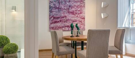 A dining area with a round table, four grey upholstered chairs, a green vase, and a purple abstract painting on the wall.