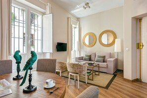 A modern living room with a round table, two chairs, a sofa, and a coffee table. There are two wall-mounted mirrors and a television.