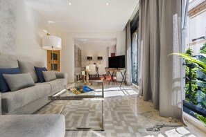 A modern living room with a sofa, coffee table, and a TV. There is a large window with curtains, a lamp, and a painting on the wall. - Genteel Home Vinuesa II (Seville)