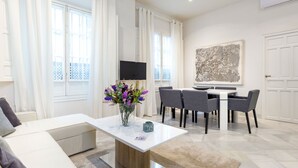 A modern living room with a white sofa, a dining table with chairs, a TV, and a large abstract painting on the wall. - Genteel Home Galera I (Seville)
