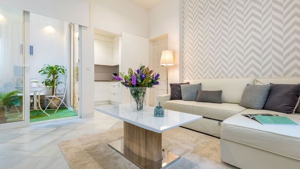 A modern living room with a glass coffee table, a sofa, and a dining area with chairs and a plant. - Genteel Home Galera I (Seville)