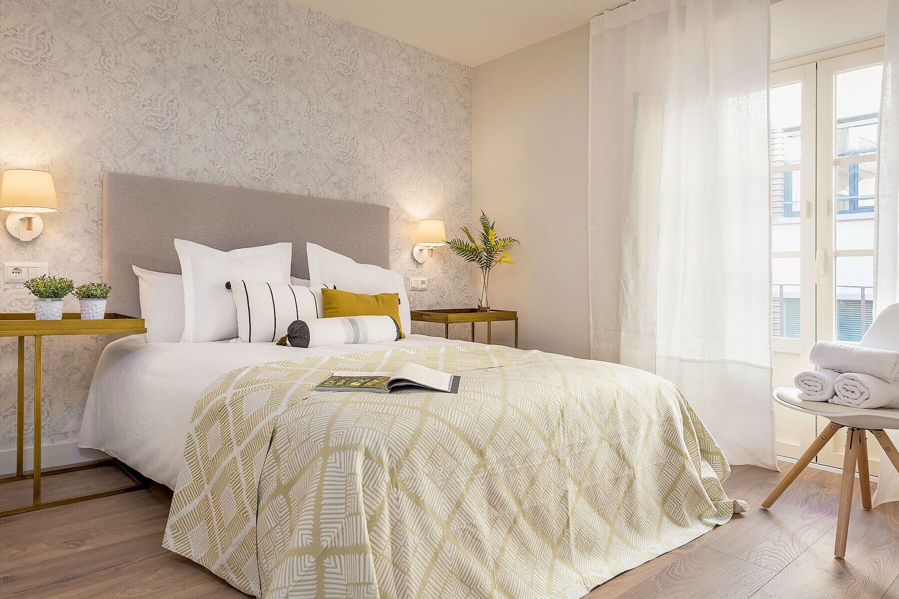 A hotel room with a bed, two bedside tables, a nightstand, a chair, and a window with curtains.