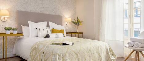 Habitación de hotel con una cama, dos mesitas de noche, una silla y una ventana con cortinas.