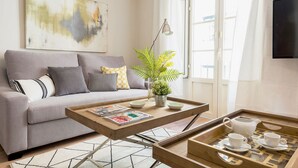 Un salon comprenant un canapé, une table basse avec des magazines, une plante et un plateau avec des tasses et une carafe.