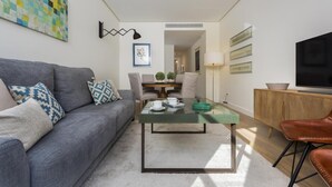 Ein modernes Wohnzimmer mit einem grauen Sofa, einem Glastisch und einem Fernseher auf einer Holzkommode.
