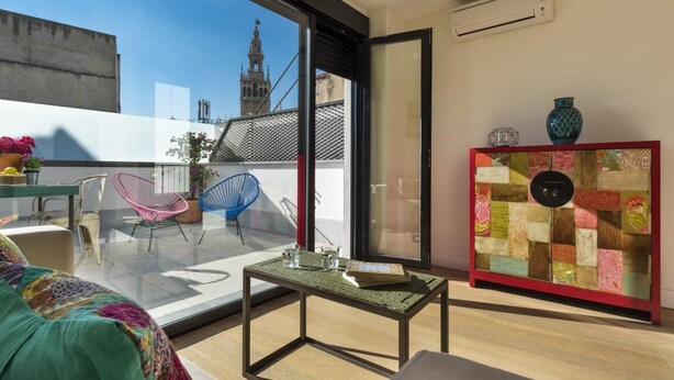 Ein modernes Wohnzimmer mit Glastür zum Balkon, einem farbenfrohen Sofa, einem kleinen Tisch und einem dekorativen Schrank.