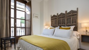 Ein Hotelzimmer mit einem großen Bett, einem hölzernen Kopfteil, einem kleinen Tisch und einem Fenster mit Vorhängen.