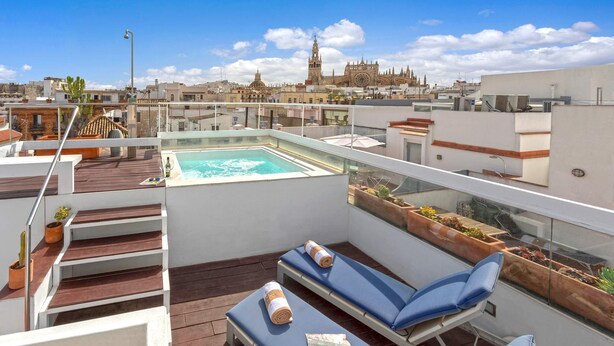 A rooftop terrace with a swimming pool, lounge chairs, and a view of a historic cathedral. - Genteel Home Real de la Carreteria (Seville)