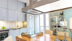 A modern kitchen with a glass-top dining table, stainless steel appliances, and a glass-fronted display cabinet. - Genteel Home Real de la Carreteria (Seville)