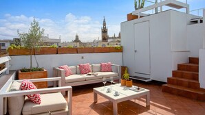 A rooftop terrace with a white sofa, red patterned cushions, a coffee table, and potted plants. - Genteel Home Real de la Carreteria (Seville)