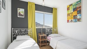 A bedroom with two beds, a window with curtains, a wall art piece, and a small table with a lamp. - Rooftop Funchal - By Wehost (Funchal)