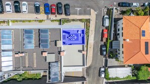 An aerial view of a parking lot with several cars, a building with solar panels, and a blue sign indicating a covered parking area. - Rooftop Funchal - By Wehost (Funchal)