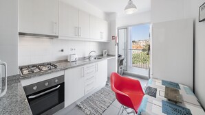 A modern kitchen with white cabinets, a gas stove, and a red chair. - Rooftop Funchal - By Wehost (Funchal)