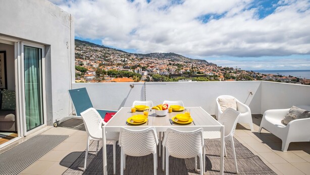 A rooftop terrace with a table set for dining, white wicker chairs, and a view of a coastal town. - Rooftop Funchal - By Wehost (Funchal)