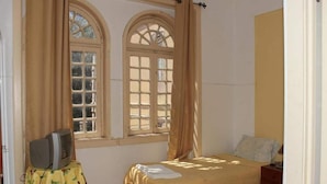 Une chambre avec deux lits, un téléviseur posé sur une petite table et de grandes fenêtres avec des rideaux.
